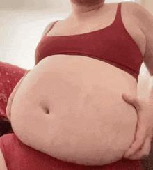 a woman in a red bra and red underwear is holding her very fat belly .