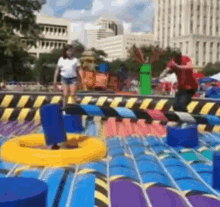 a man and a woman are playing a game on a colorful inflatable mat in a park .
