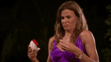 a woman in a purple dress is making a funny face while holding a red and white object .