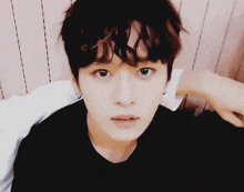 a close up of a young man with curly hair wearing a black shirt and earrings .