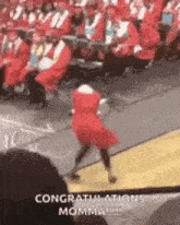 a woman in a red dress is dancing in front of a crowd of graduates at a graduation ceremony .