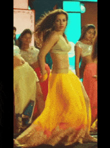 a woman in a yellow skirt is dancing in front of a group of people
