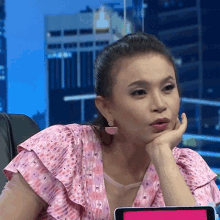 a woman in a pink dress is sitting in a chair with her hand on her face .