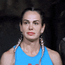 a woman with braids wearing a blue tank top looks at the camera
