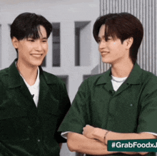 two men in green shirts are standing next to each other with their arms crossed