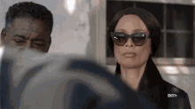 a woman wearing sunglasses stands next to a man with bet written on the bottom right