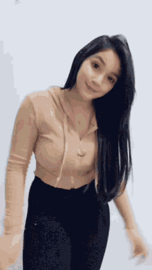 a woman with long black hair is wearing a tan hoodie and black pants