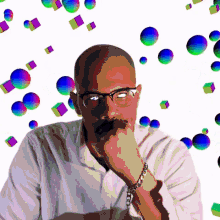 a man wearing glasses and a chain bracelet is surrounded by colorful balls and cubes