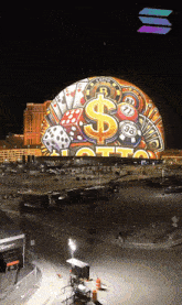 a large globe with a dollar sign dice and playing cards on it is lit up at night