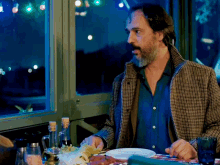 a man with a beard sits at a table with a plate of food in front of him