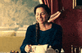a woman is sitting at a table with a cup of coffee and a teapot