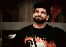 a man with a beard is smiling and wearing a black t-shirt with flames on it