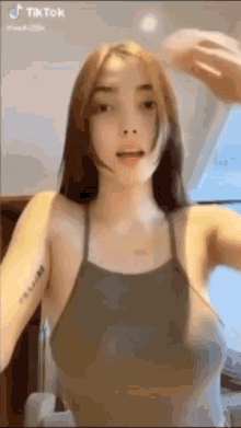 a woman in a tank top with a tattoo on her arm is standing in front of a mirror .