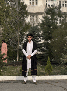 a man wearing a white shirt and a black scarf stands in front of a building