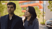 a man and a woman are standing next to each other in front of a building that has trt1 on it