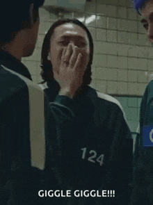 a man in a squid game uniform is covering his mouth with his hand while laughing .