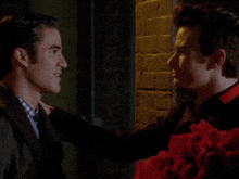 a man holds a bouquet of red roses while another man looks on