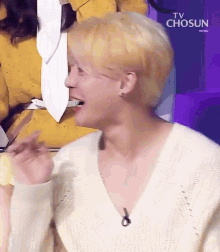 a man with blonde hair is wearing a white sweater and earrings .