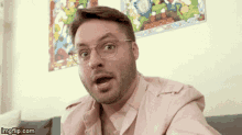 a man wearing glasses and a pink shirt is sitting on a couch .