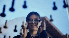 a woman wearing glasses is standing in front of a chess board .