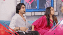 a man and a woman are sitting on a couch . the woman is wearing a pink dress .