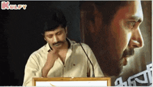 a man is standing at a podium in front of a microphone with a picture of a man in the background .