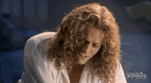 a man with long curly hair is wearing a white shirt and looking down at something .