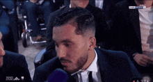 a man in a suit and tie is talking into a microphone while sitting at a table