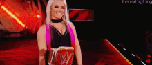 a woman with blonde hair and pink highlights is holding a wrestling championship belt and smiling .