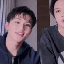 two young men are sitting next to each other in a room . one of the men is wearing a blue hoodie .