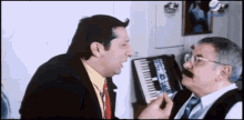 a man in a suit and tie is talking to another man in front of a piano keyboard
