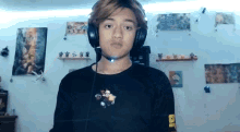 a young man wearing headphones and a black shirt is standing in front of a wall with pictures on it .