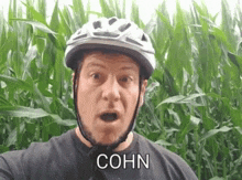 a man wearing a helmet and a black shirt is standing in front of a corn field .