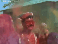a man is covered in red powder and laughing while standing in front of a crowd of people .