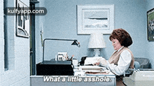 a woman is sitting at a desk in an office with a typewriter and a lamp .
