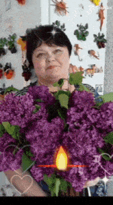 a woman is holding a large bouquet of purple flowers in front of a refrigerator