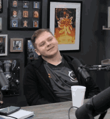 a man sitting in front of a microphone with a picture on the wall behind him that says ' avengers ' on it