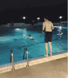 a man stands on the edge of a swimming pool watching another man swim