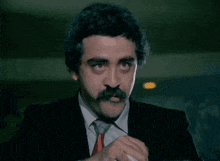 a man with a mustache is wearing a black suit and tie