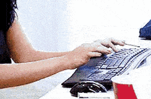 a woman is typing on a keyboard next to a cup of coffee .