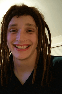 a young man with dreadlocks is smiling and wearing a green shirt