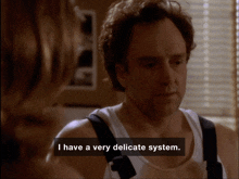 a man in a white tank top is talking to a woman and says i have a very delicate system