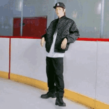 a young man is standing on a ice rink wearing a hat and a jacket .