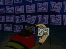 a cartoon character is holding a piece of paper in front of a wall of drawings .