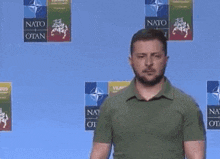 a man with a beard is standing in front of a blue wall with logos for nato .