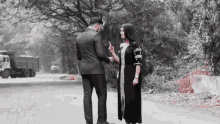 a man in a suit and a woman in a black dress are standing next to each other on the side of a road