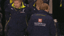 a man wearing a blue jacket that says mansion.com casino & poker