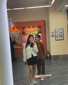 two people taking a selfie in front of a photoism color sign
