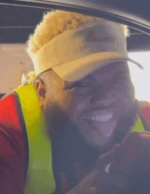 a man wearing a visor and safety vest is sticking his tongue out while driving a car