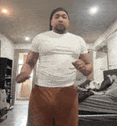 a man in a white shirt and brown shorts is standing in front of a bed